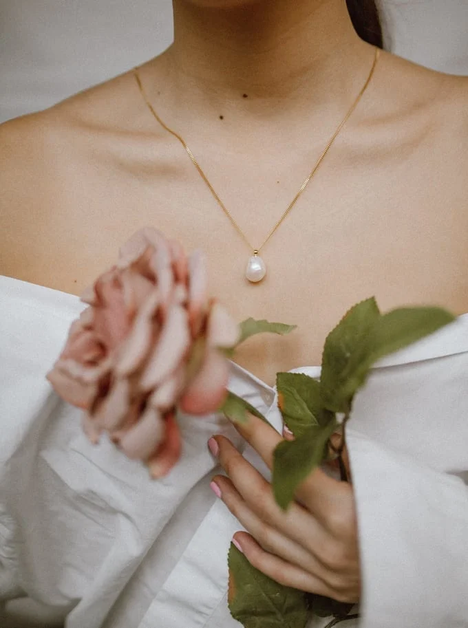 A woman holding flowers in her hand and wearing pearls.