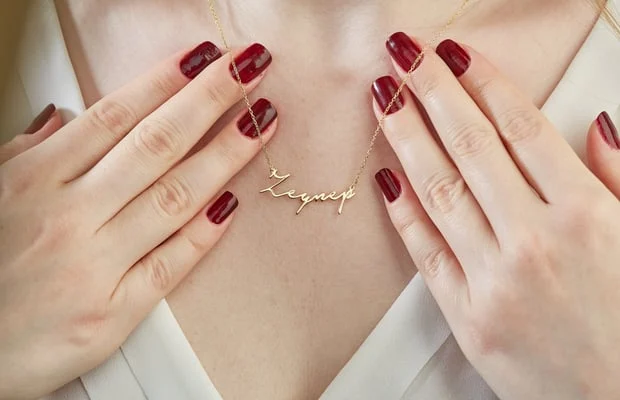 A woman with red nails holding up her necklace.