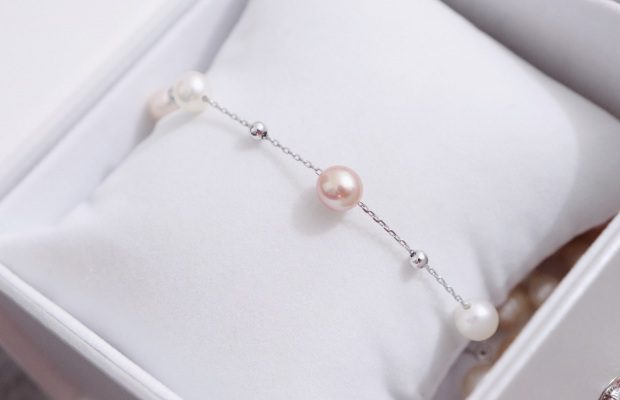 A white box with a pink pearl and silver chain bracelet.